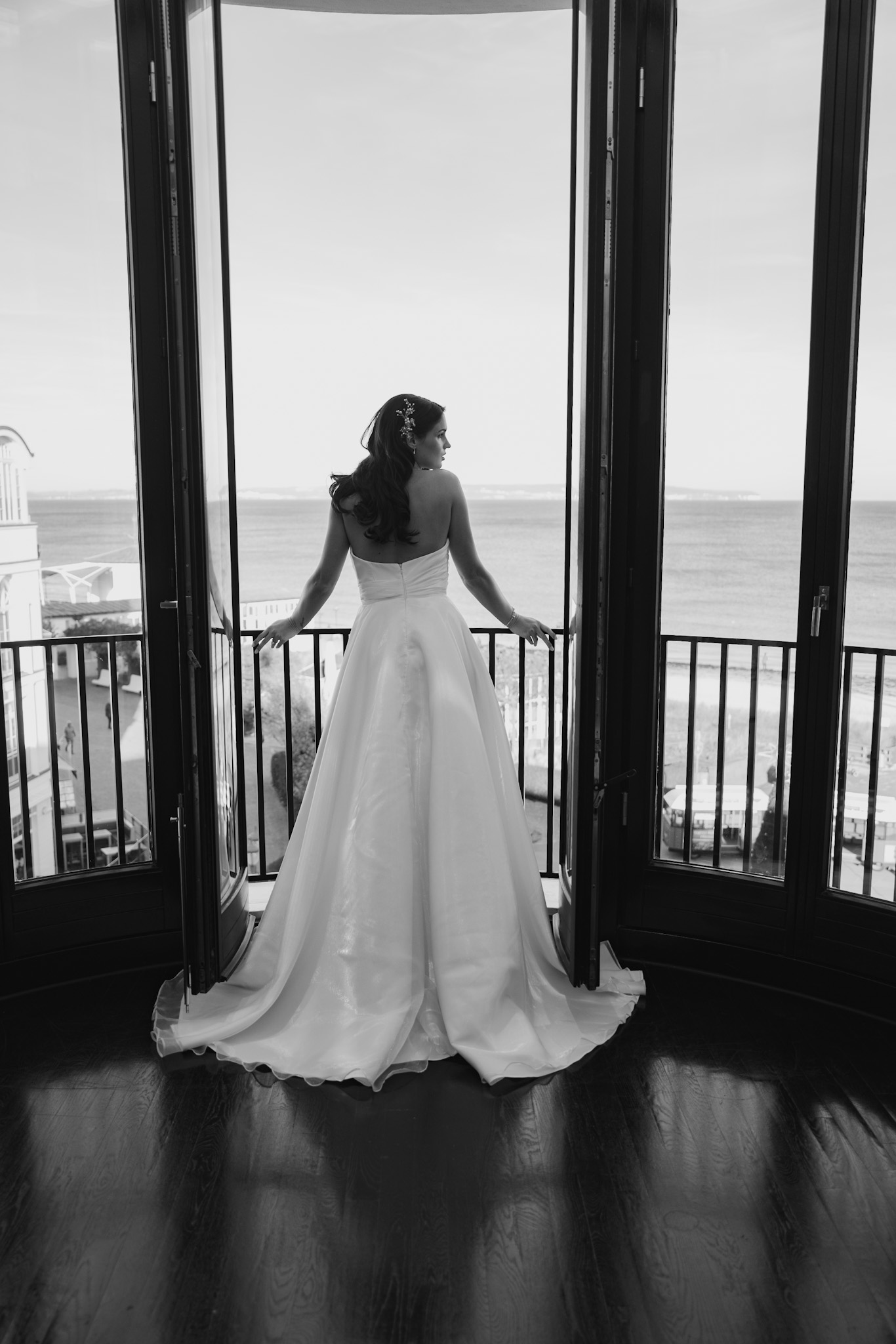 Eine Braut im Brautkleid steht an der offenen Balkontür, blickt auf das Meer und träumt von ihrem perfekten Tag mit Hilfe eines Hochzeitsplaners auf Sylt.