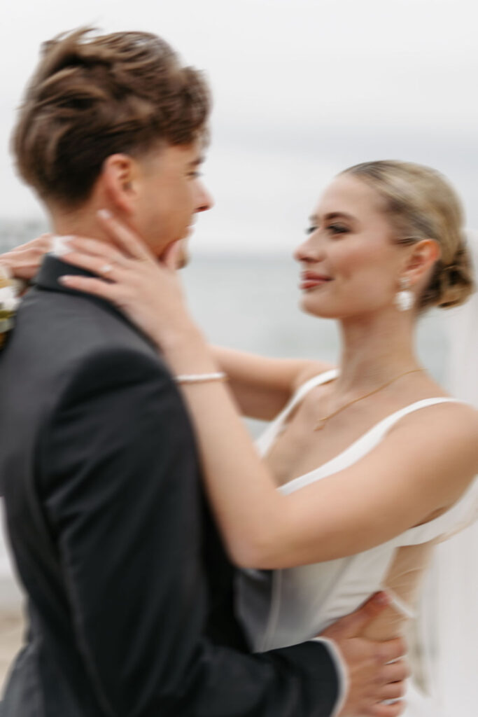 Braut und Bräutigam umarmen sich und lächeln sich an ihrem Hochzeitstag an. Mit Hilfe eines Hochzeitsplaners wird ein magischer Moment an der Ostsee festgehalten.