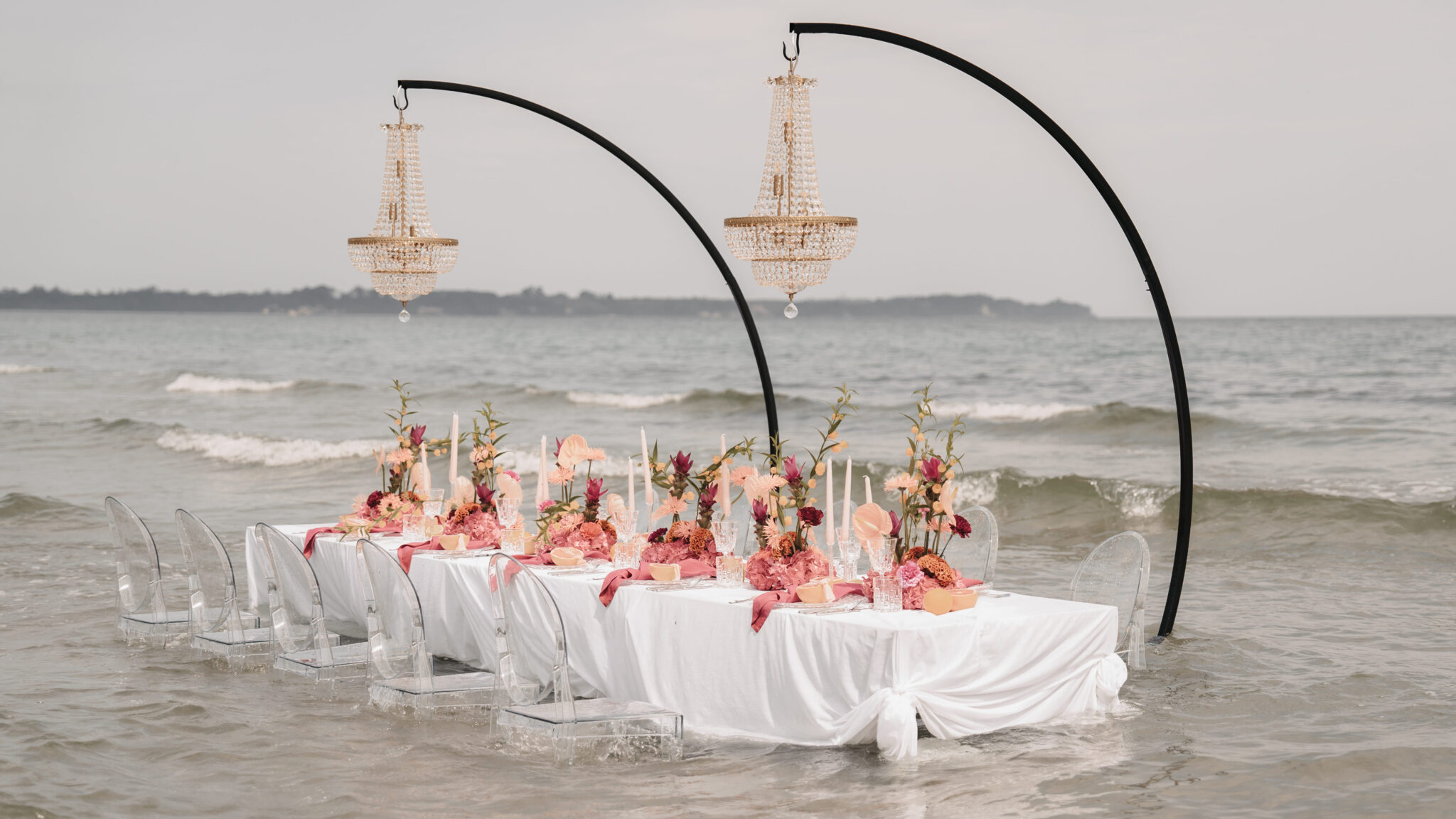 Eleganter Tisch mit Blumen und Kronleuchtern im Meer, Wellen um die weiße Tischdecke und Stühle - perfekt für eine Traumfeier bei einem Hochzeitsplaner auf Sylt.