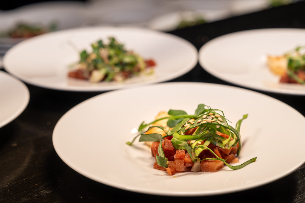 Ein weißer Teller mit einem Feinschmeckersalat mit Mikrogrün und Sesam, unscharfe Teller im Hintergrund.