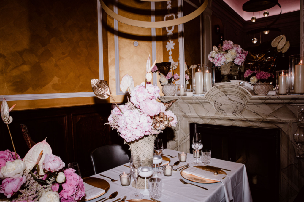 Eleganter Esstisch mit rosa und weißem Blumenschmuck, Kerzen und goldenen Akzenten in einem luxuriösen Ambiente.