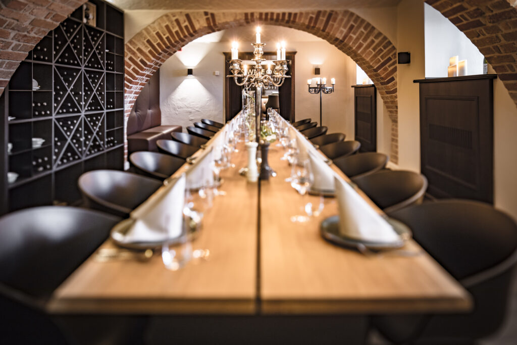 Ein langer Esstisch, gedeckt für ein formelles Essen in einem gemütlichen, gewölbten Backsteinzimmer mit eleganter Beleuchtung.