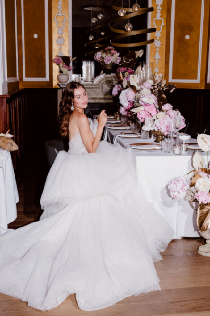 Die Braut in einem weißen Hochzeitskleid sitzt an einem eleganten Tisch, der mit rosa und weißen Blumen geschmückt ist.