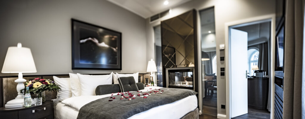 Modernes Hotelzimmer mit großem Bett, Rosenblättern, Nachttischlampen und Blick auf eine angrenzende Sitzecke.